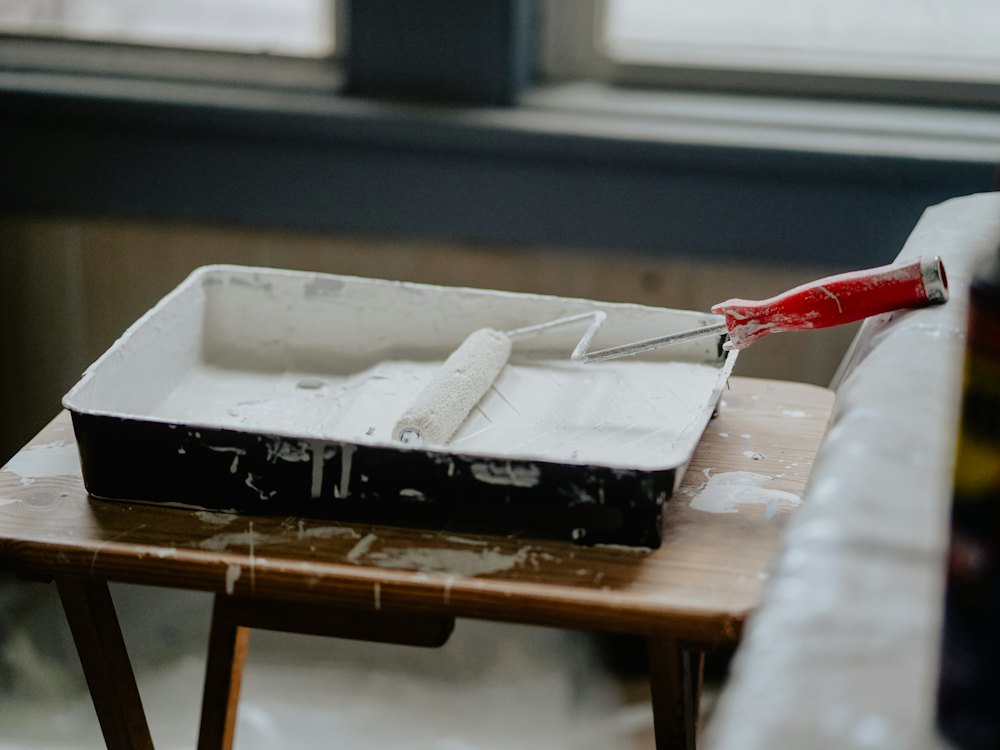 Paint roller resting in a tray of white paint